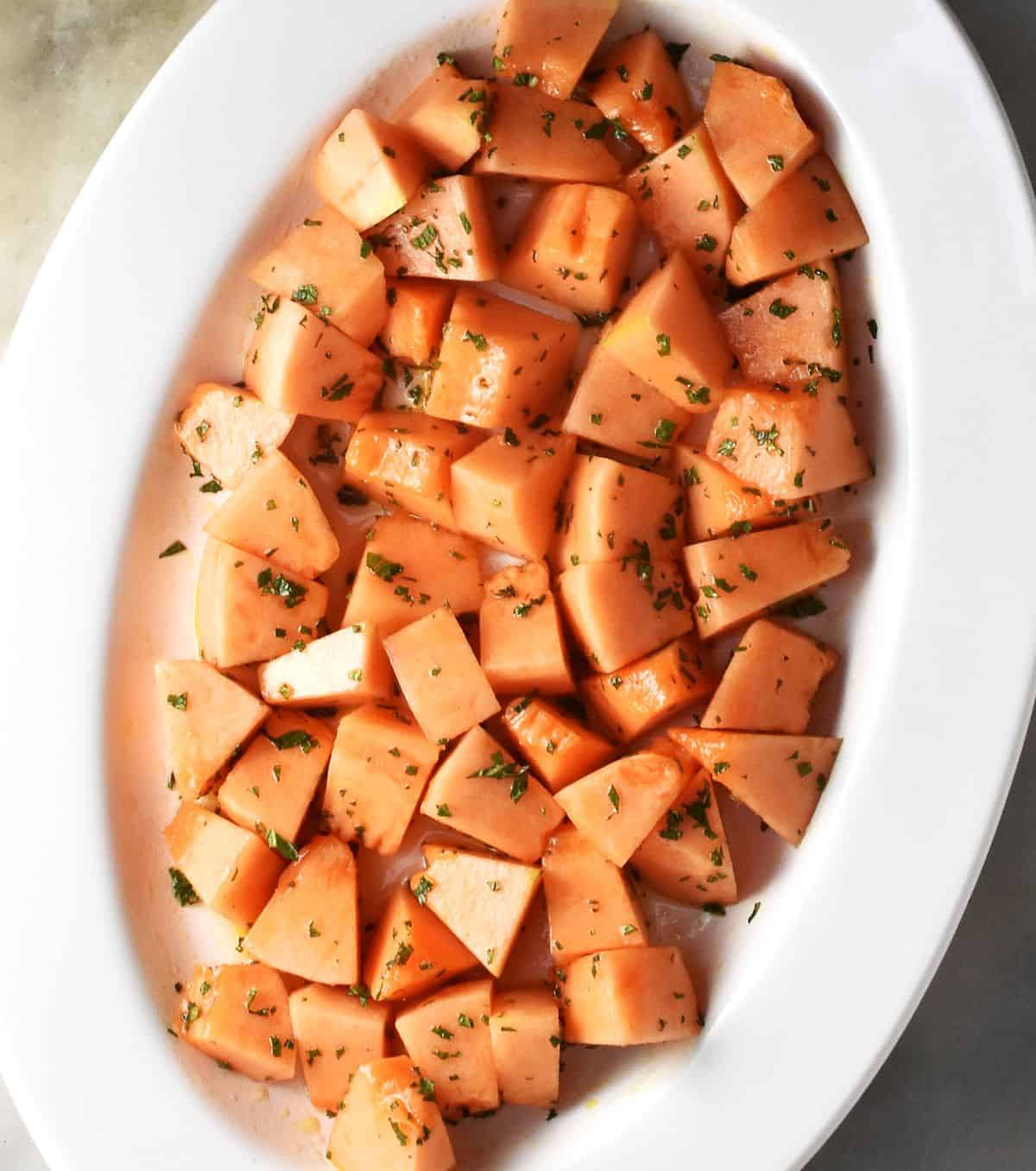 Close-up view of fresh cantaloupe pieces with dressing and mint on white platter.