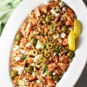Top down view of cantaloupe salad with feta, olives and lemon wedges on white oval platter.