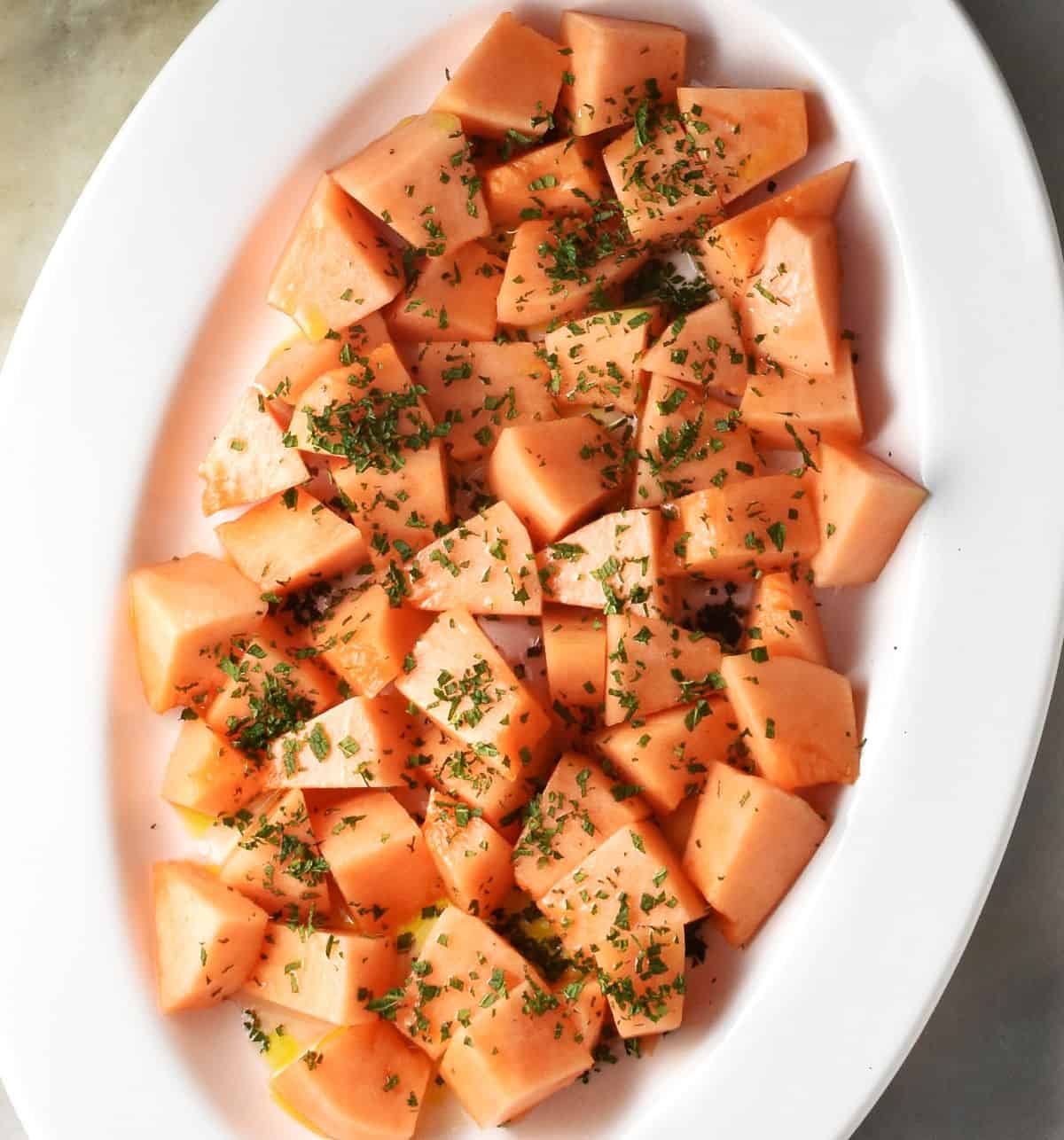 Top down view of cubed cantaloupe with chopped mint on white oval plate.
