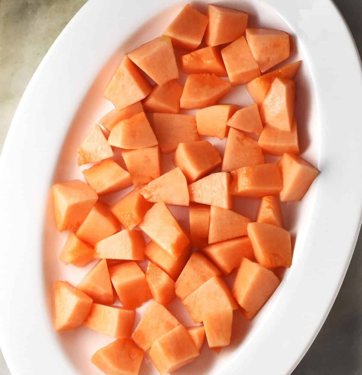 Top down view of cubed peeled cantaloupe on white plate.