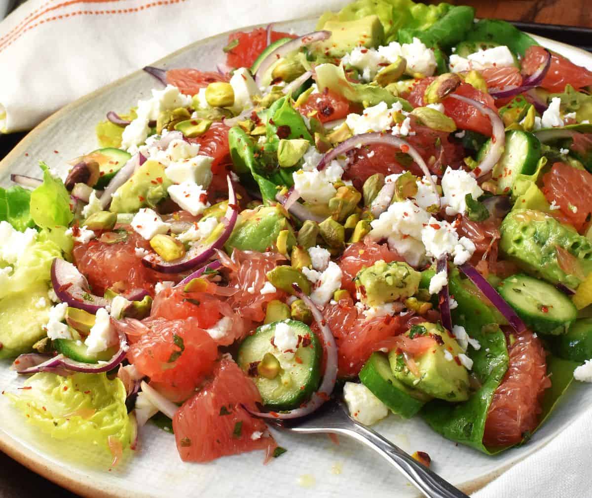 Side view of grapefruit and avocado salad with feta on white plate with fork.