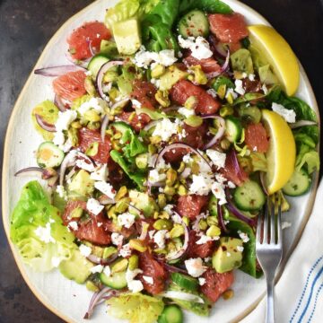 Top down view of grapefruit salad with avocado, cucumber and feta on white, oval plate.