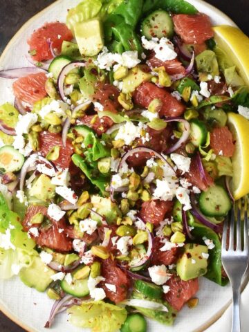 Top down view of grapefruit salad with avocado, cucumber and feta on white, oval plate.