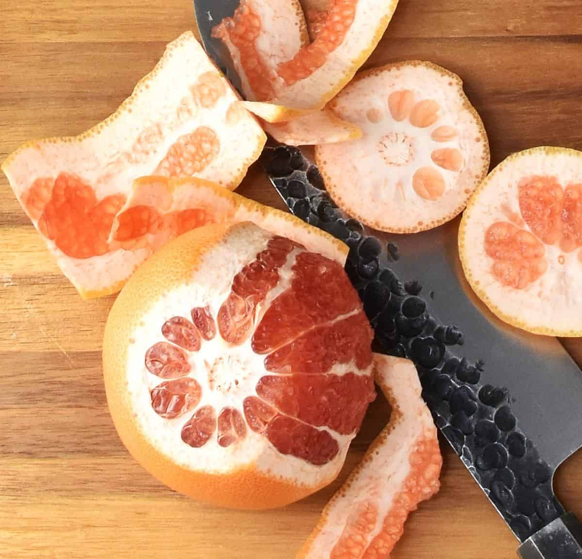 Top down close-up view of partly peeled red grapefruit on wooden board with large knife.