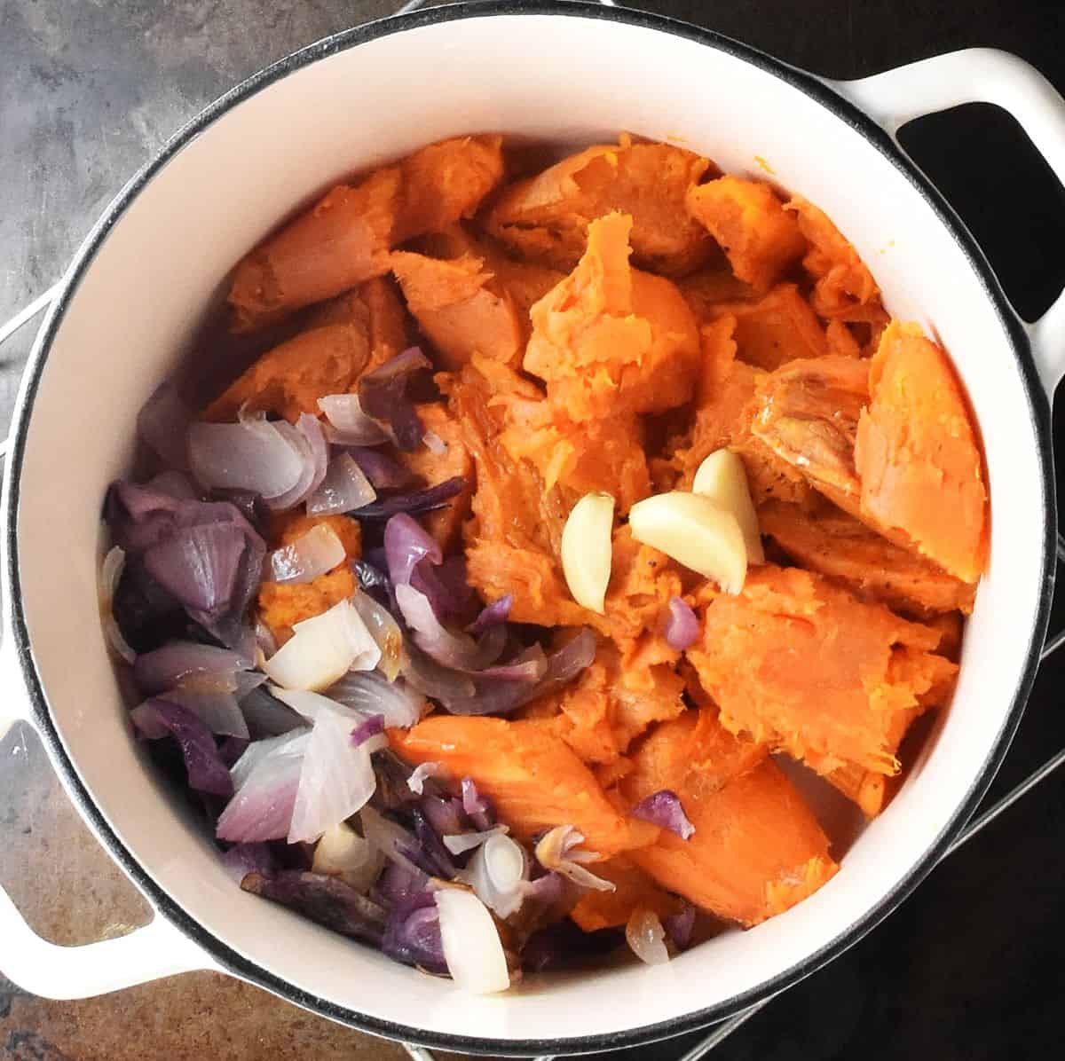Sweet potato pulp, chopped red onion and garlic in white pot.