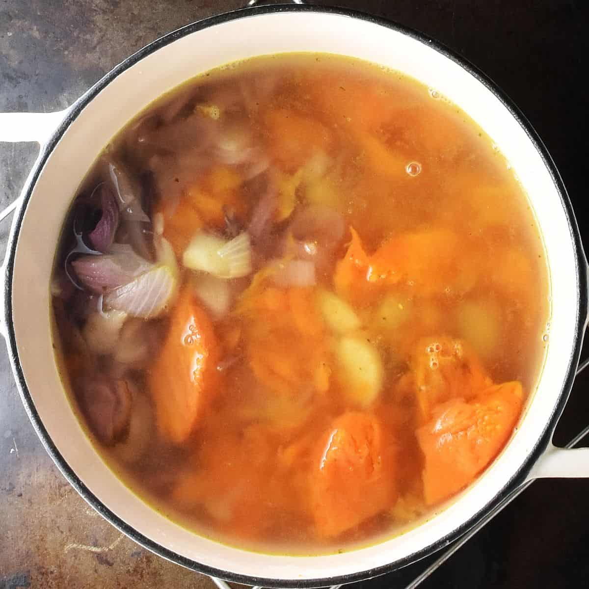 Chunks of sweet potato and onion with broth in white pot.