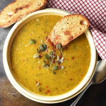 Top down view of roasted sweet potato soup garnished with fresh herbs in brown bowl with toasted bread.