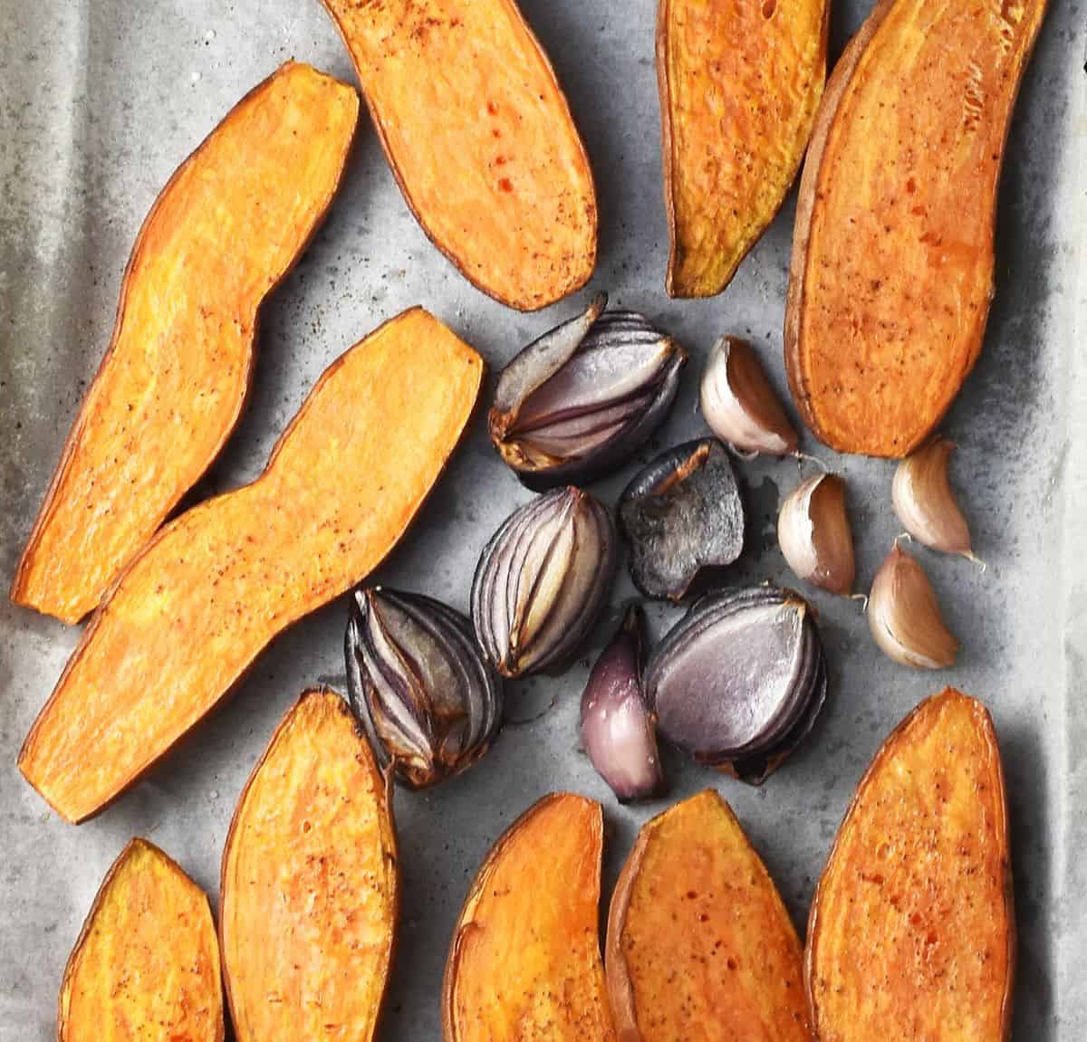 Top down view of roasted sweet potato halves and red onion pieces on parchment.