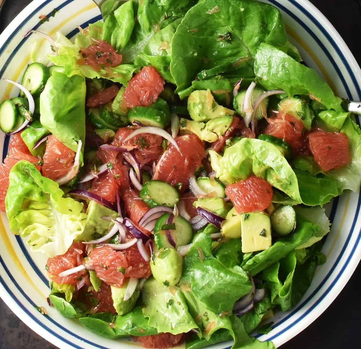 Salad leaves with chunks of grapefruit and vegetables in large, shallow bowl.