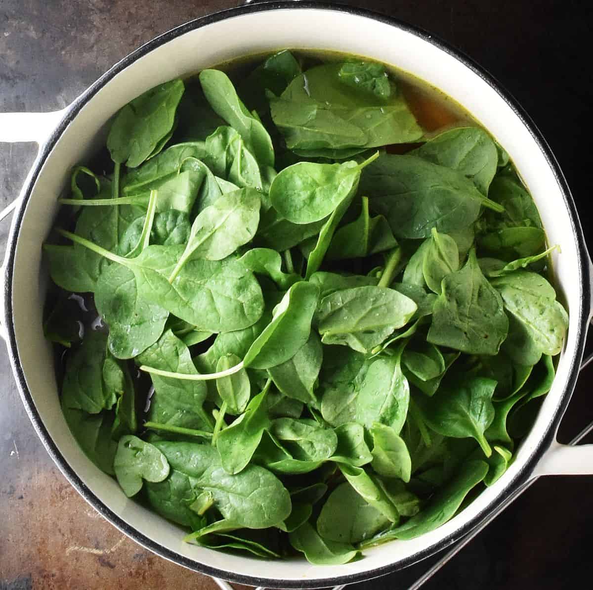 Top down view of fresh baby spinach in white pot with broth.