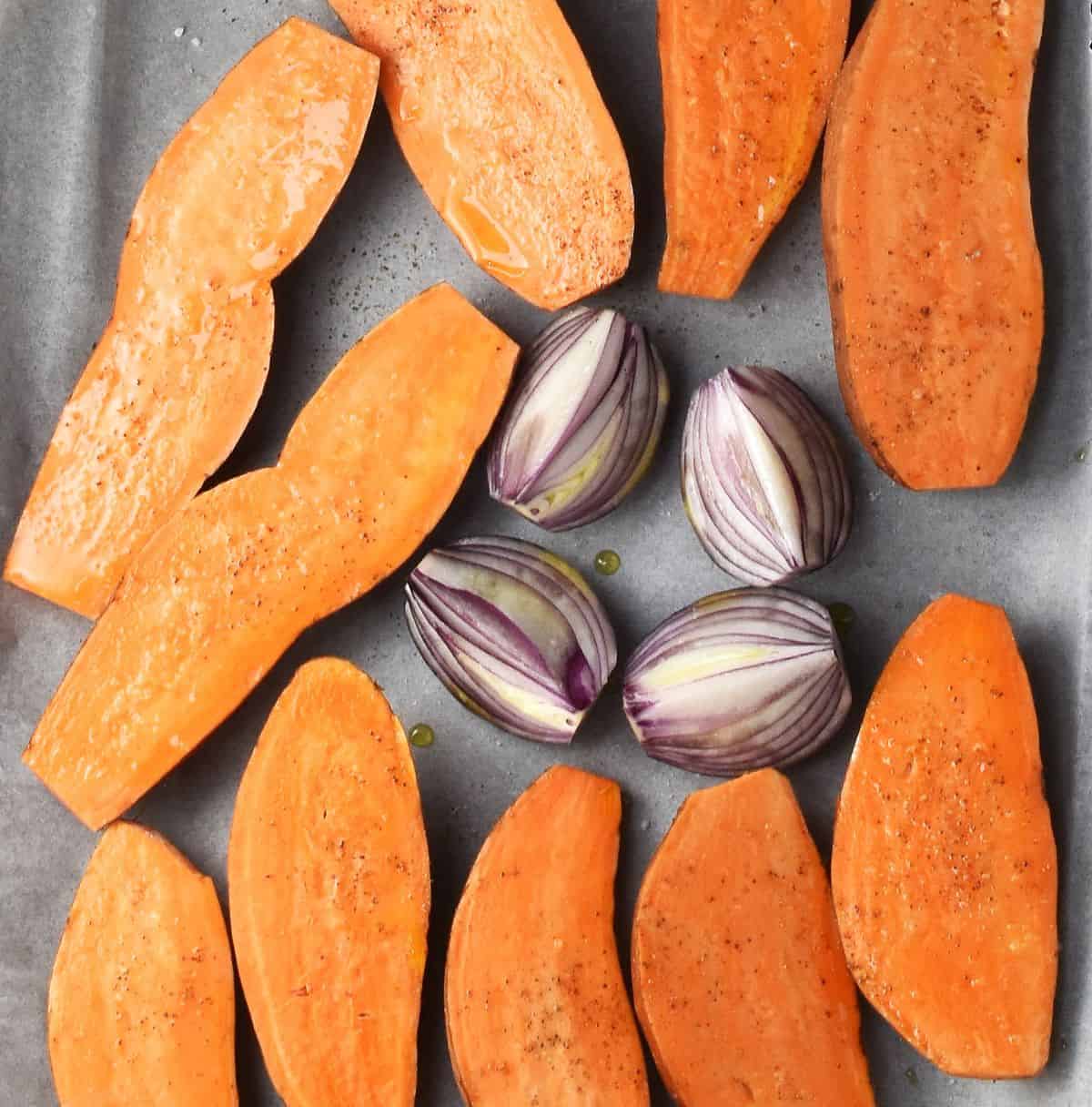 Halved sweet potatoes with red onion on top of parchment.