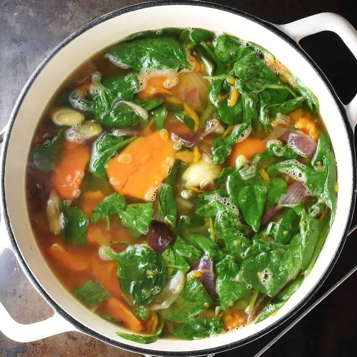 Pieces of sweet potato and fresh spinach with broth in white pot.
