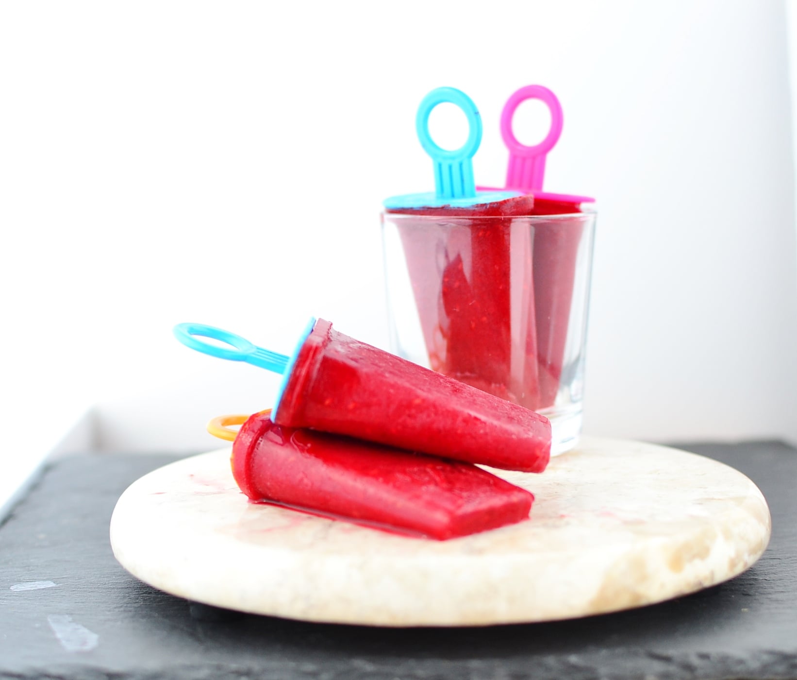 Side view of rooibos raspberry ice pops on top of marble platter and in glass.