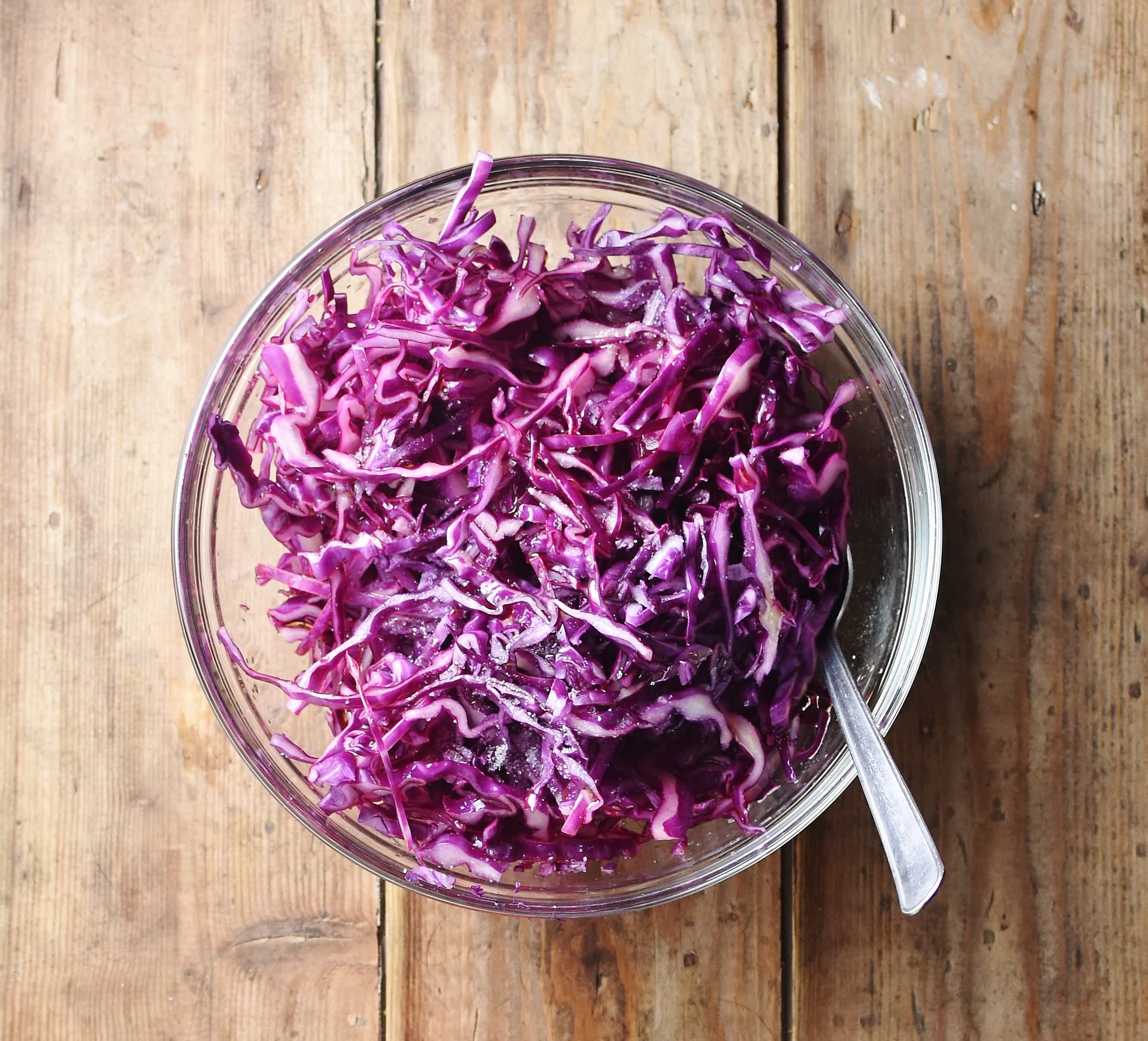Red cabbage salad with spoon in mixing bowl.