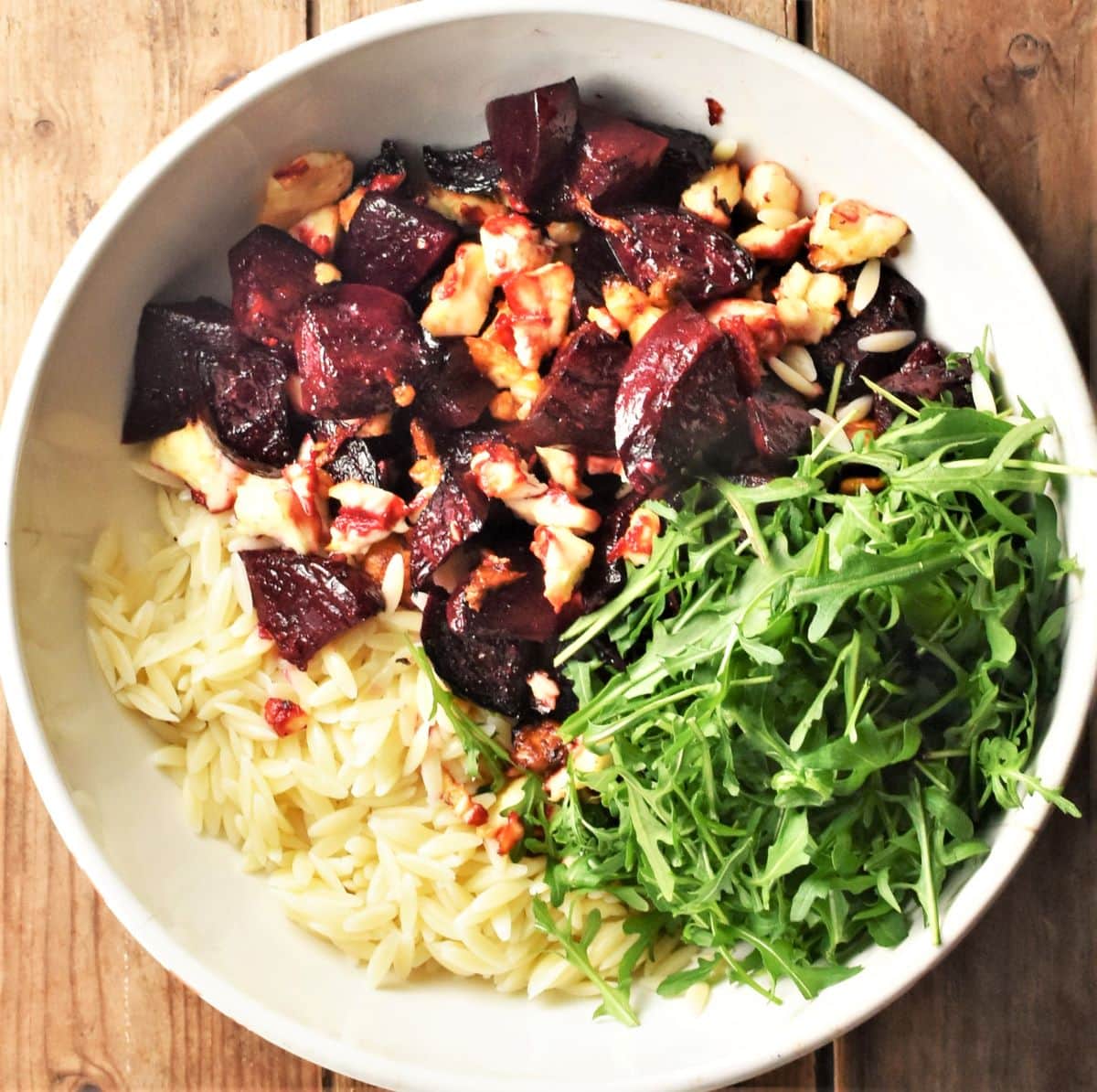 Beetroot, pasta and arugula in large white bowl.