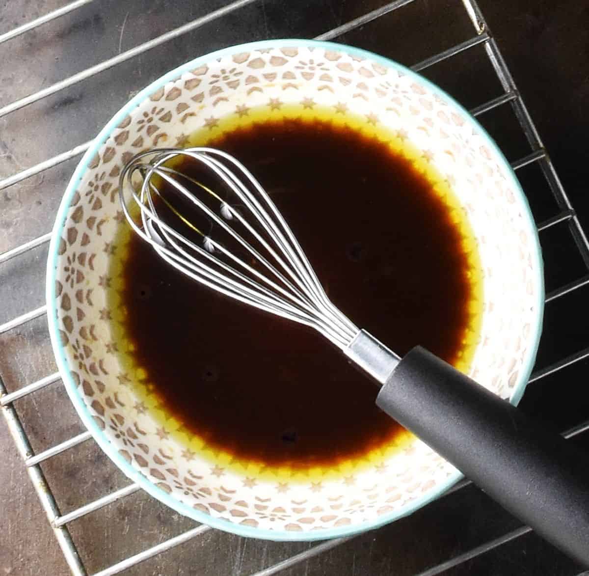 Balsamic dressing in grey bowl with small whisk.