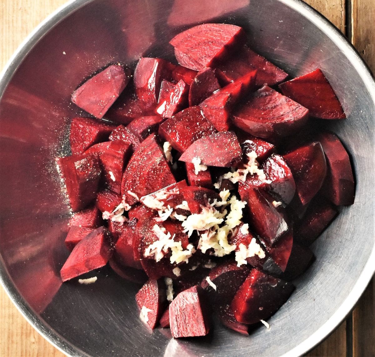 Peeled chopped beetroot with grated garlic in large metal bowl.