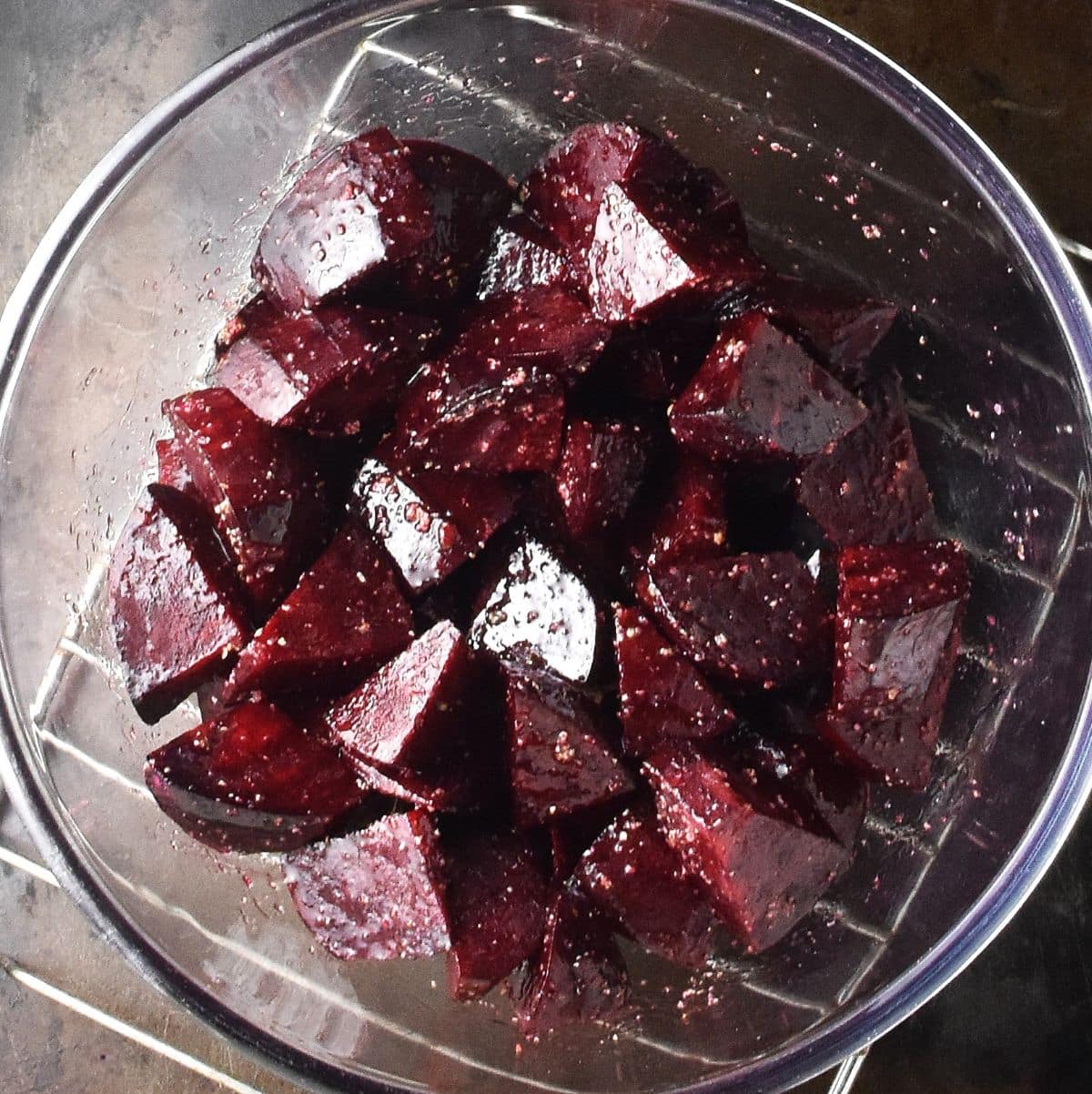 Top down view of beet chunks coated in oil in glass bowl.