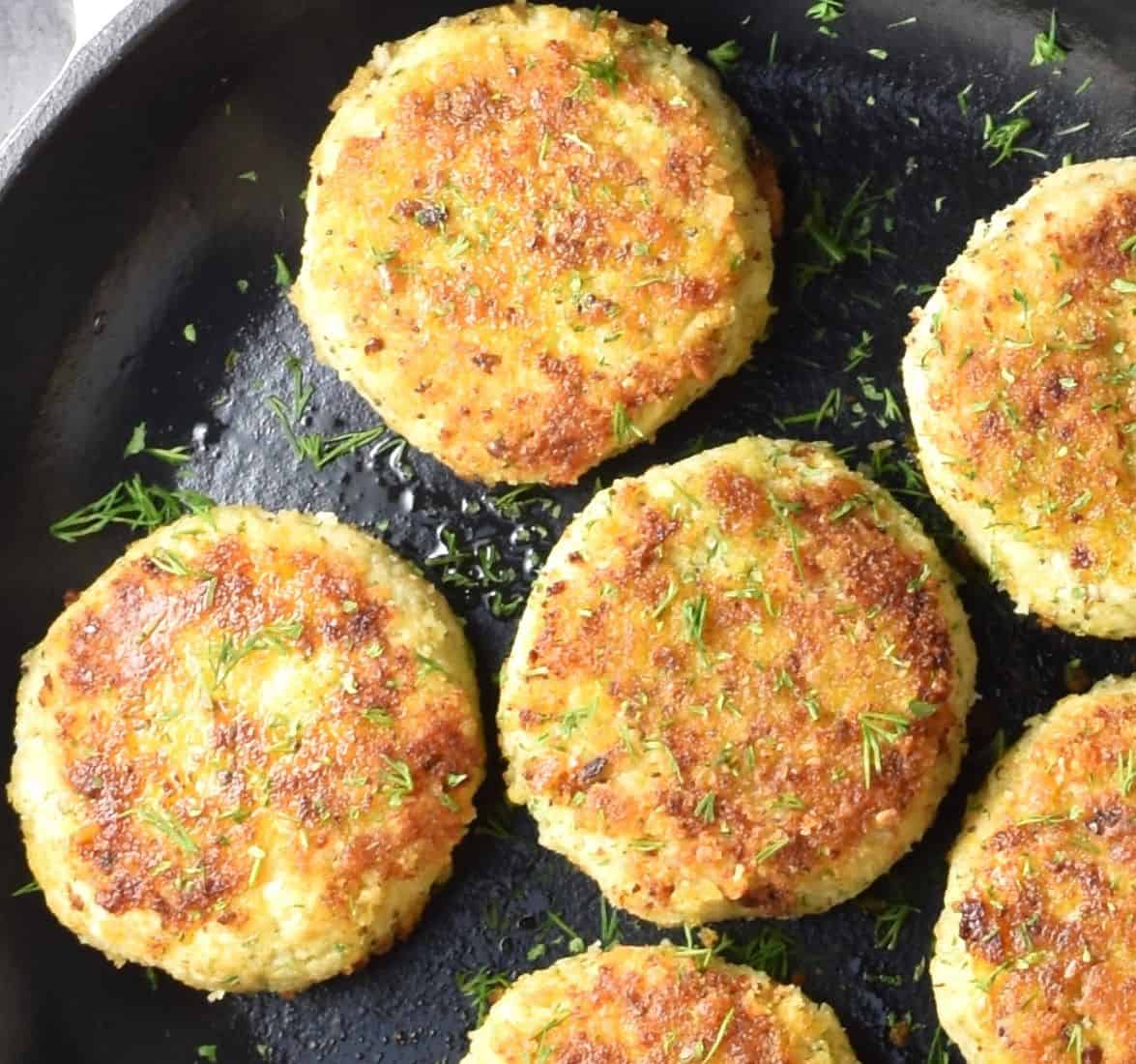 close-up view of breaded cauliflower patties in pan.