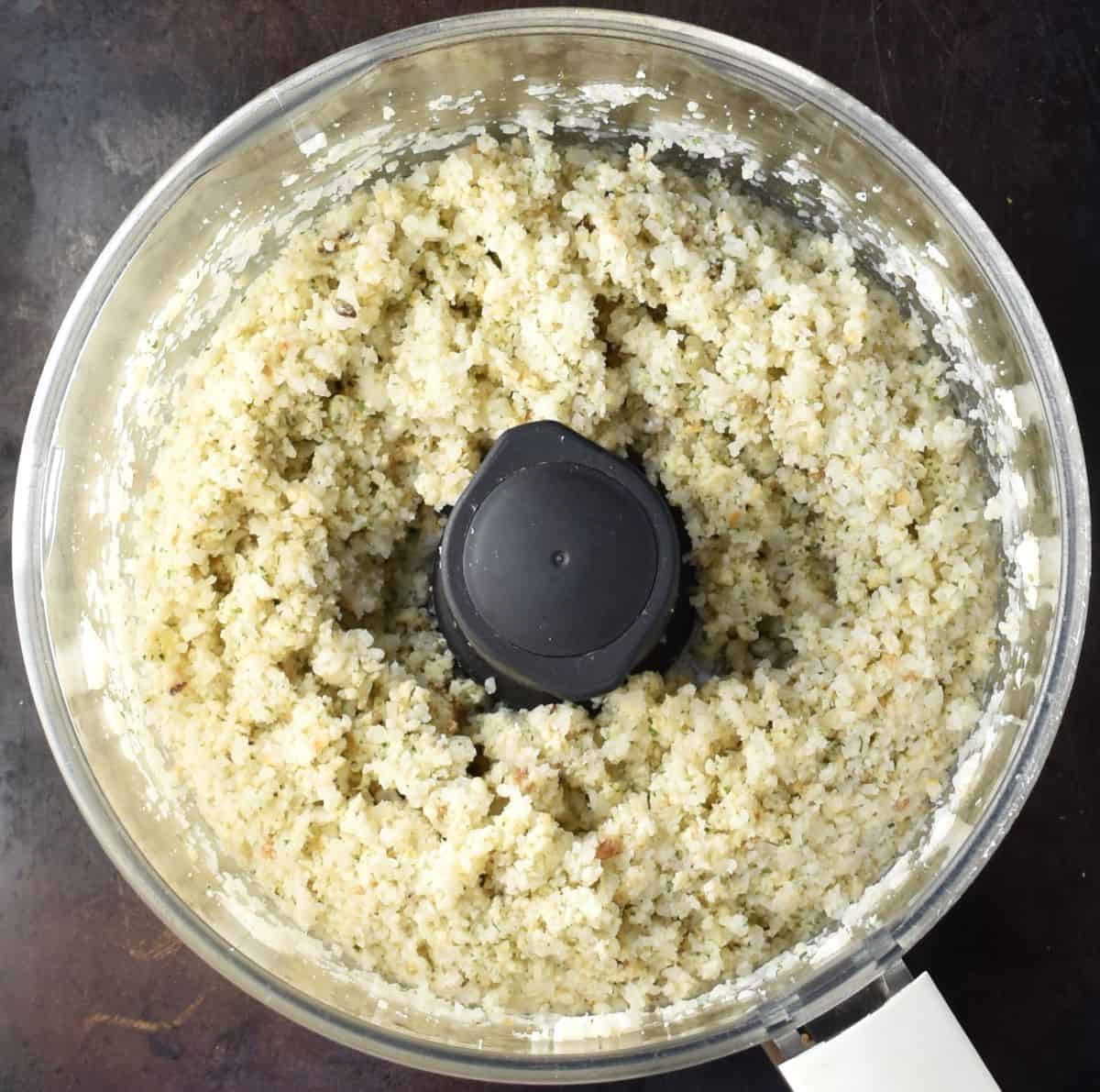 Sticky cauliflower patties mixture in food processor bowl.