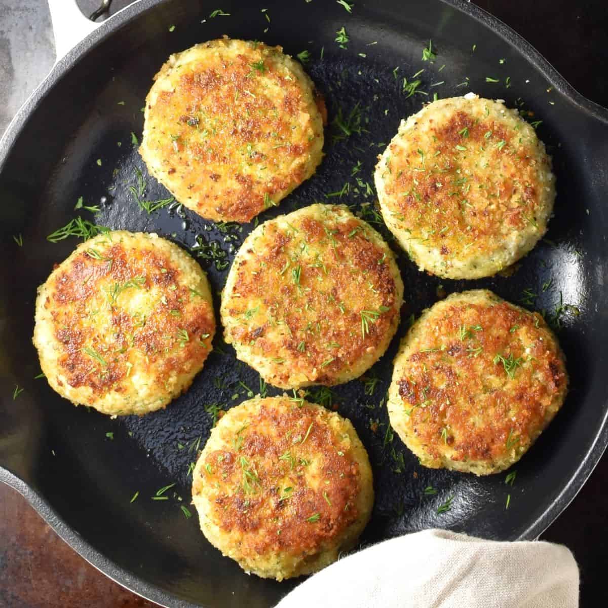 Top down view of 6 crispy cauliflower patties in pan.