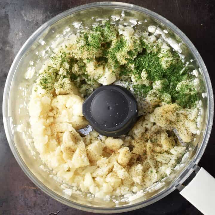 Cauliflower pieces with herbs in food processor.