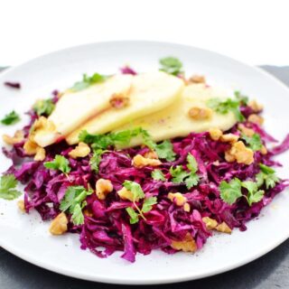 Pickled red cabbage slaw with walnuts, cilantro and pear slices on top of white plate.