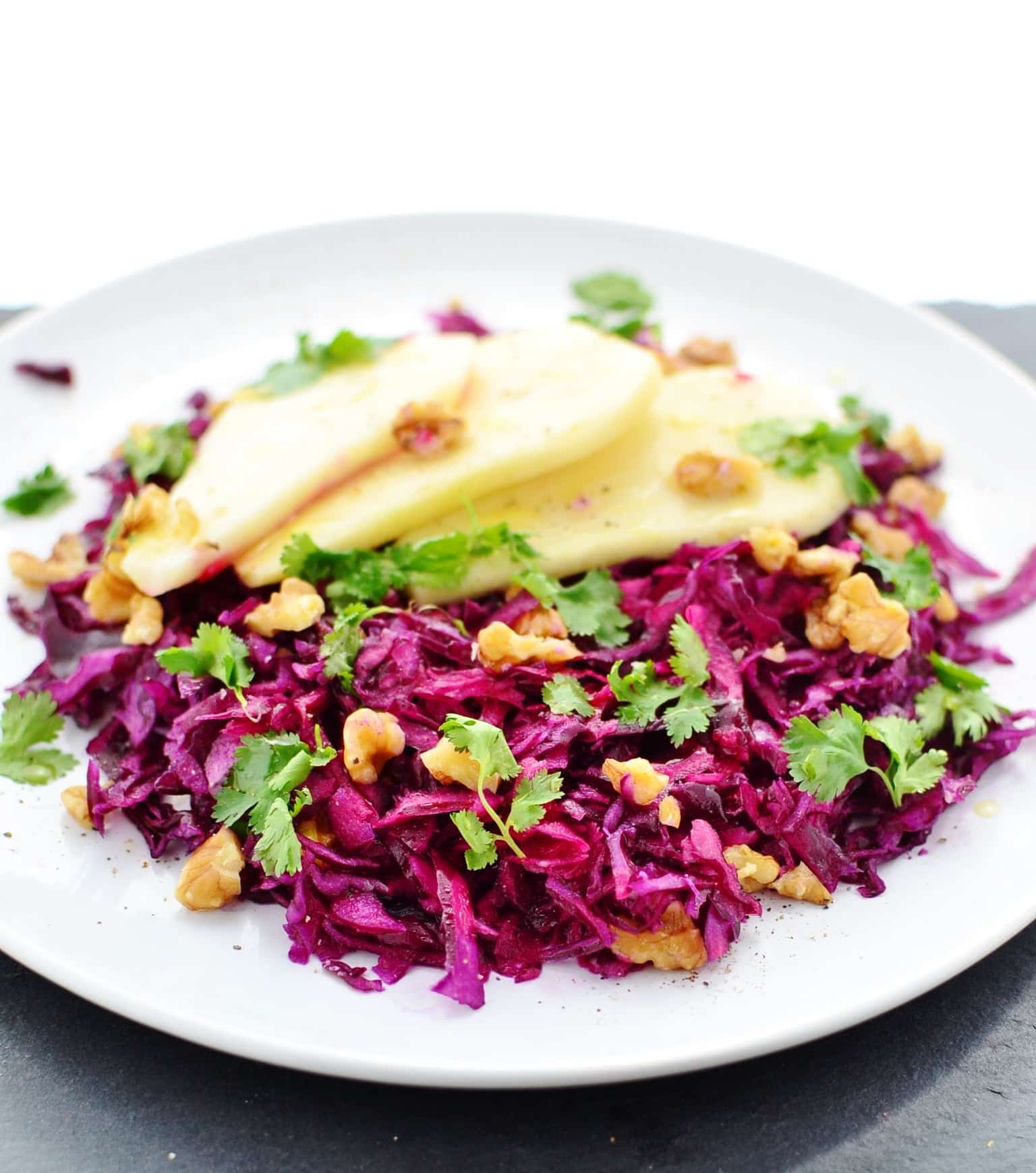 Pickled red cabbage slaw with walnuts, cilantro and pear slices on top of white plate.