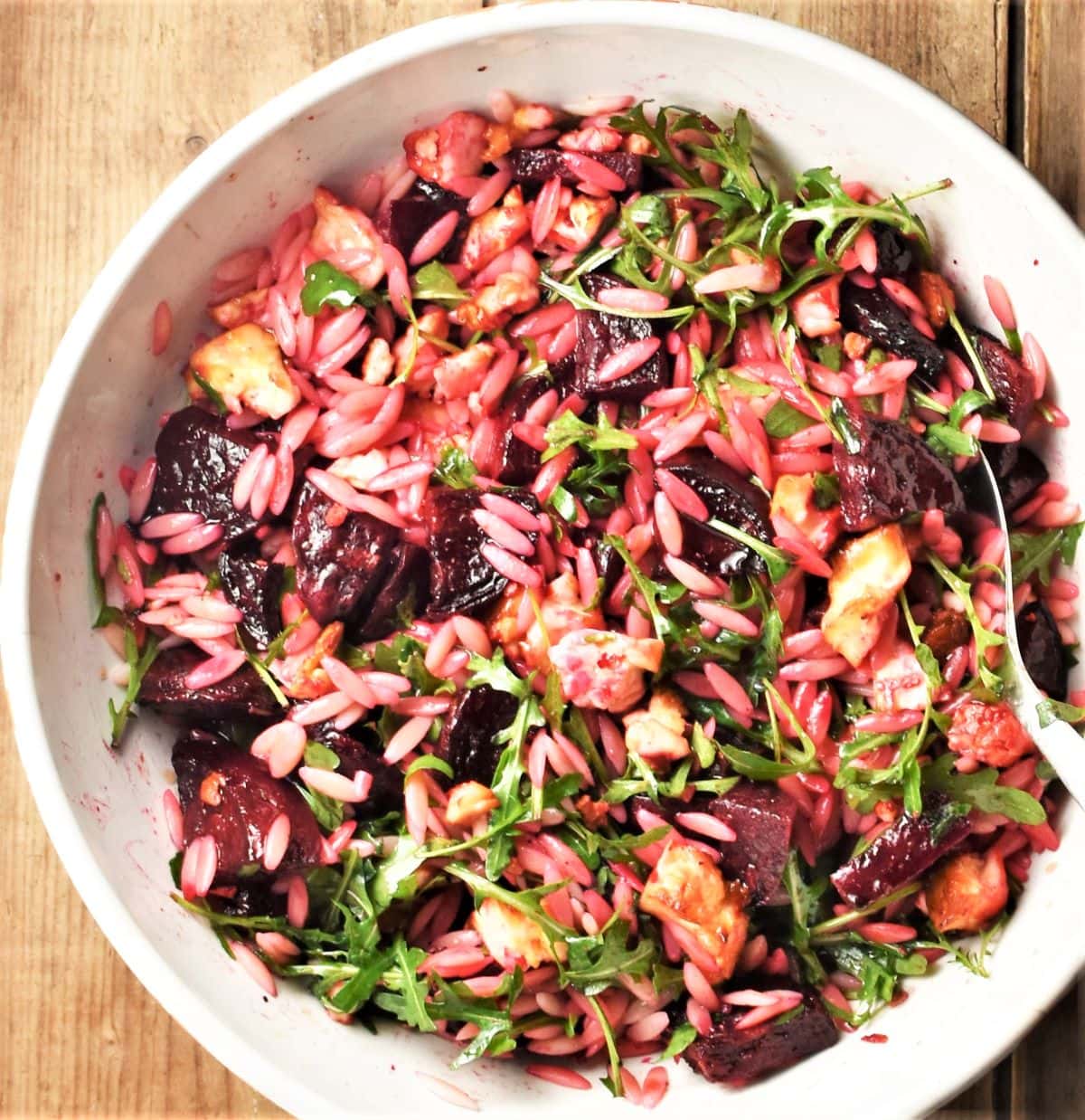 Beet and feta pasta salad with arugula in large white bowl.