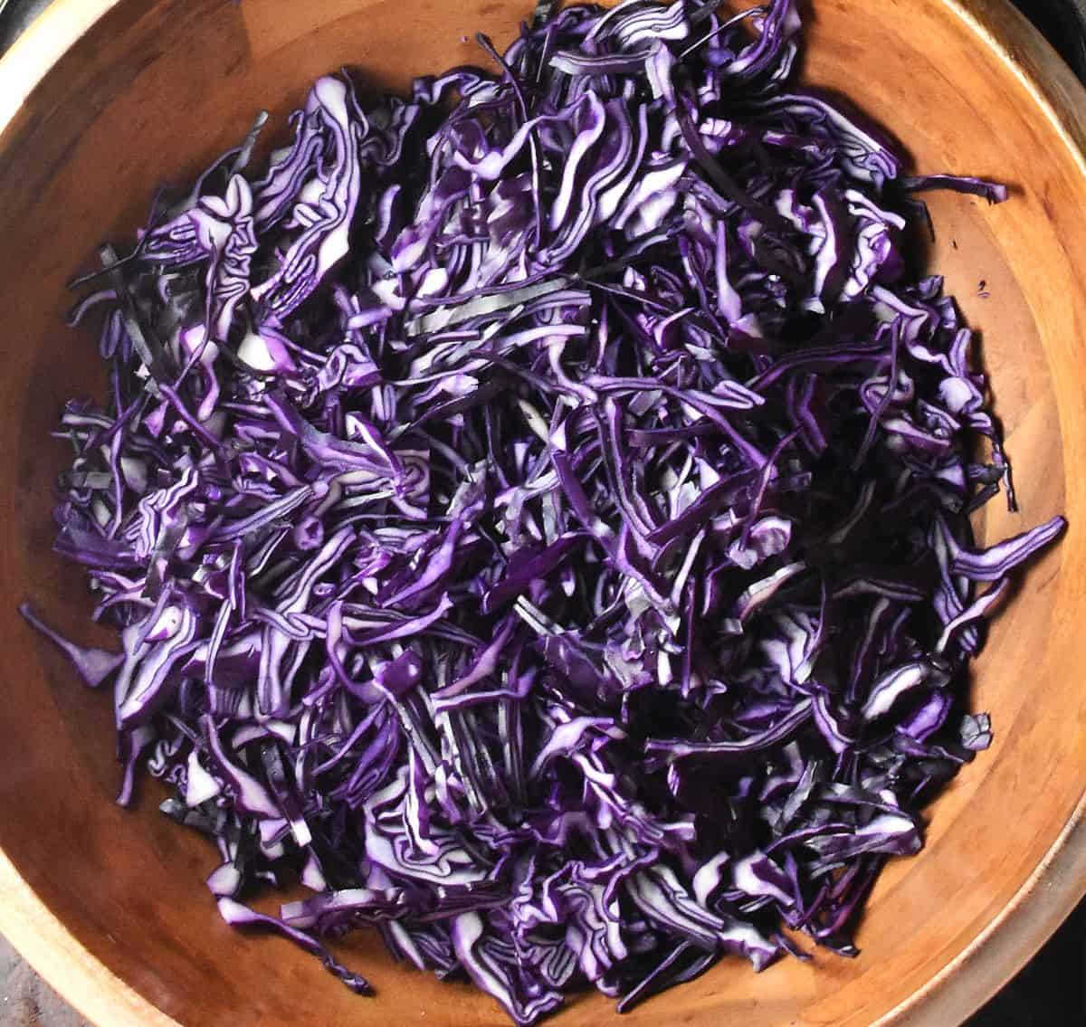 Shredded red cabbage in large wooden bowl.