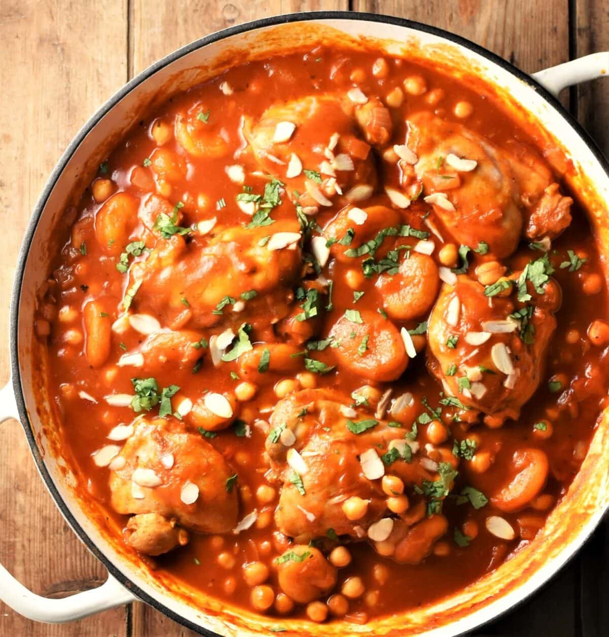 Chicken with chickpeas in tomato sauce with almond flakes in shallow white dish.