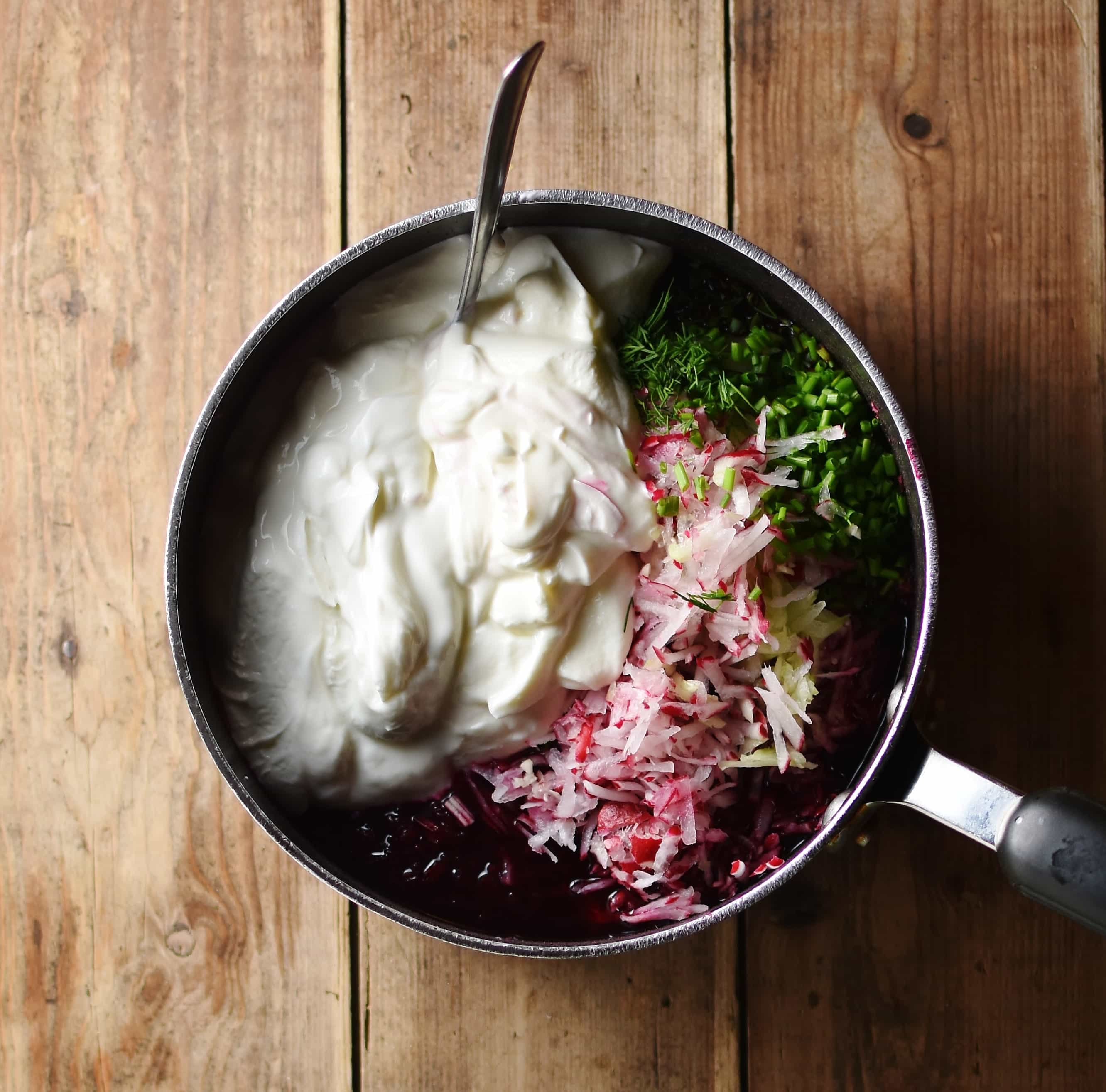 Yogurt, grated radish and chopped herbs in pot with spoon.