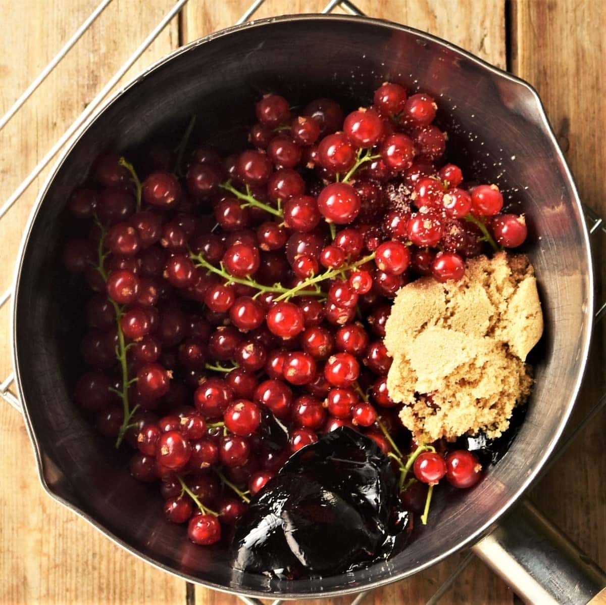 Redcurrants with stems, brown sugar and jelly in saucepan.