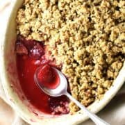 Partial top down view of vegan plum crumble with spoon in oval dish.