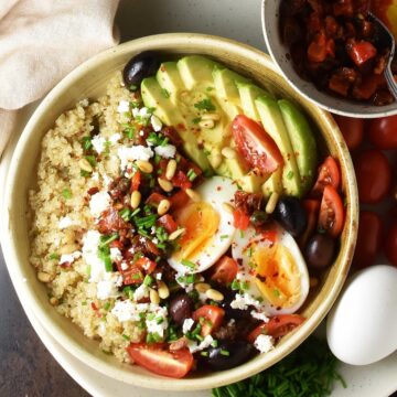 Top down view of quinoa breakfast bowl with vegetables and egg in brown shallow bowl.