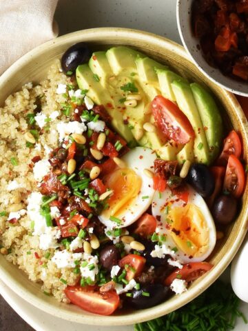 Top down view of quinoa breakfast bowl with vegetables and egg in brown shallow bowl.