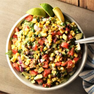 Top down view of corn salsa with lime wedges in bowl with spoon.