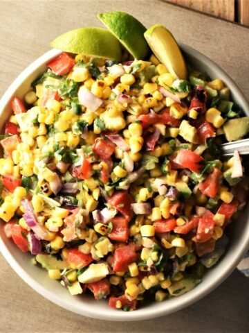 Top down view of corn salsa with lime wedges in bowl with spoon.