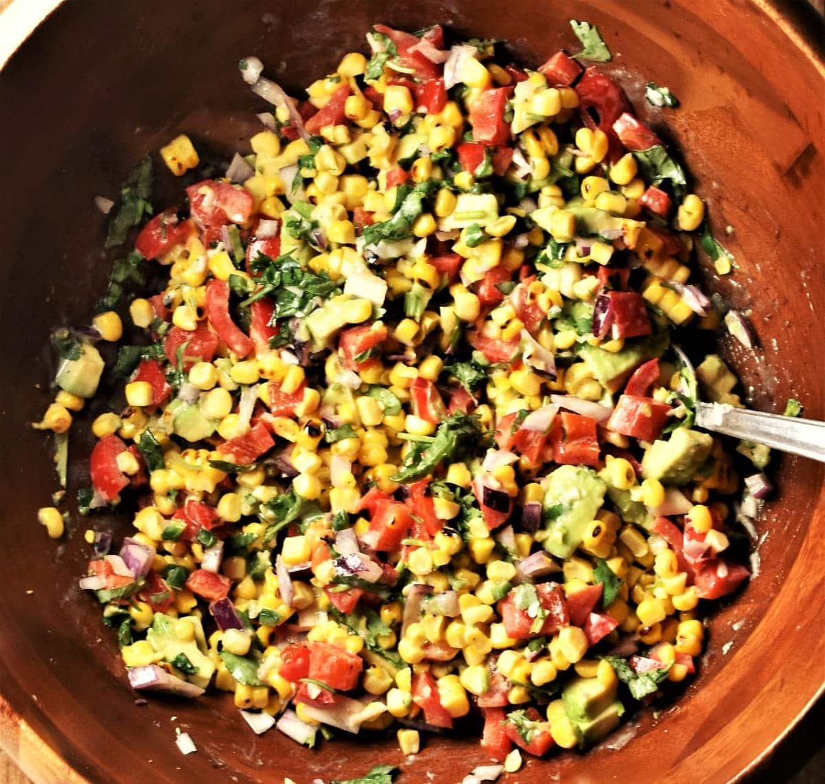 Corn and vegetable salsa in large wooden bowl with spoon.