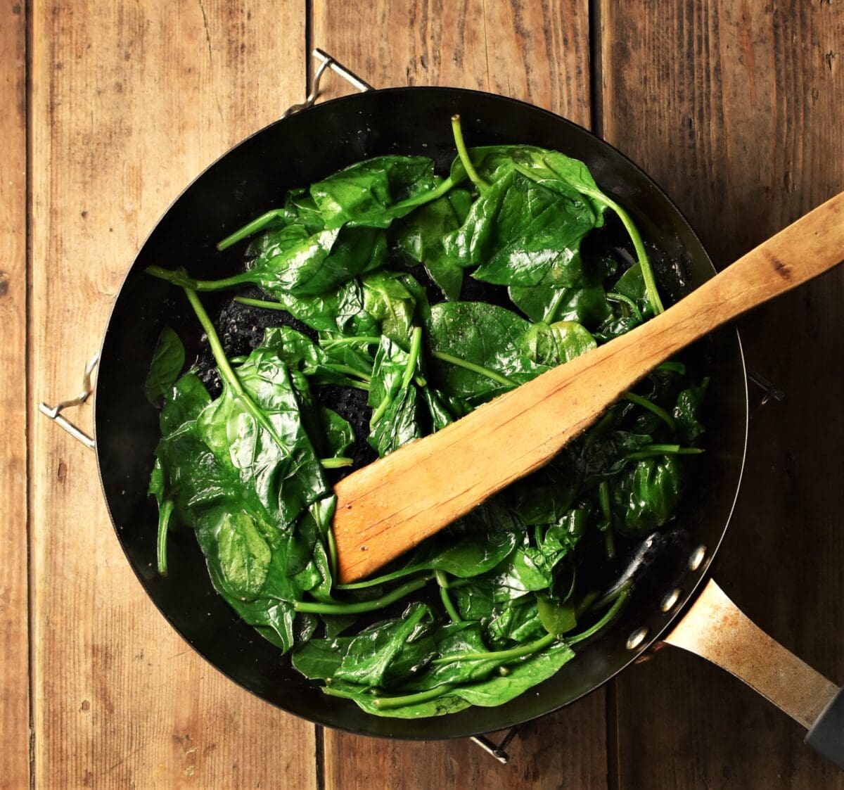 Spinach in pan with wooden spatula.