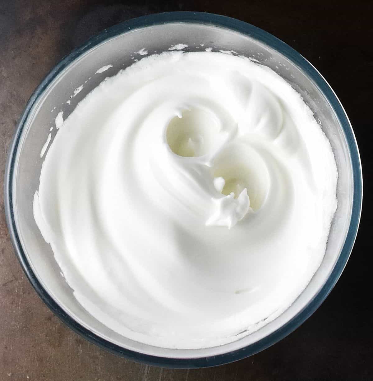 Top down view of beaten egg whites in glass bowl.