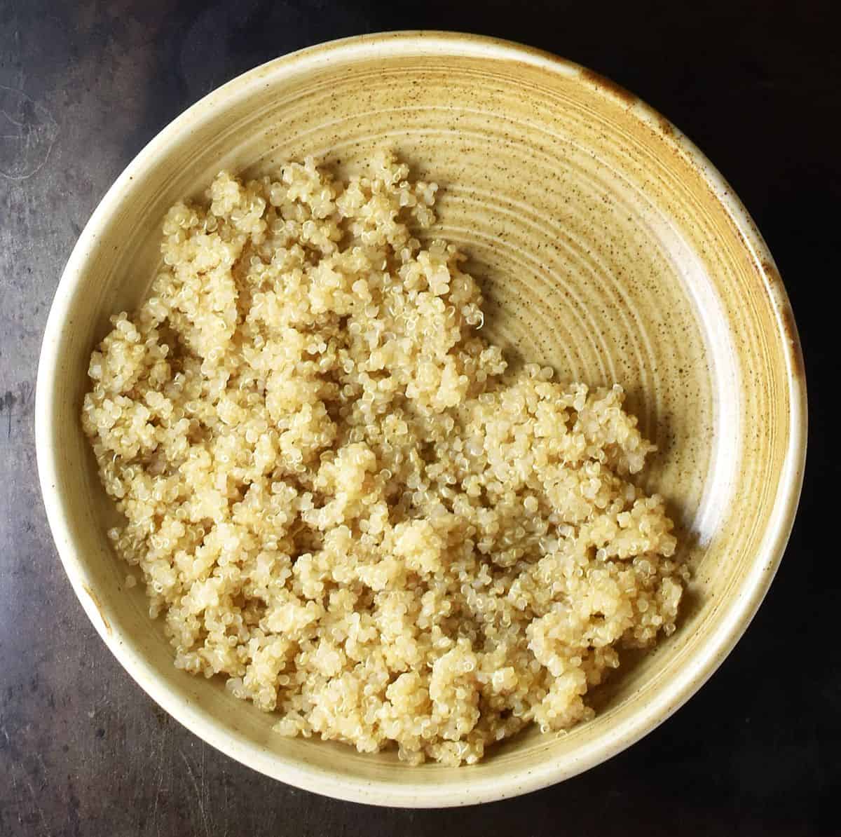 Top down view of cooked quinoa in brown bowl.