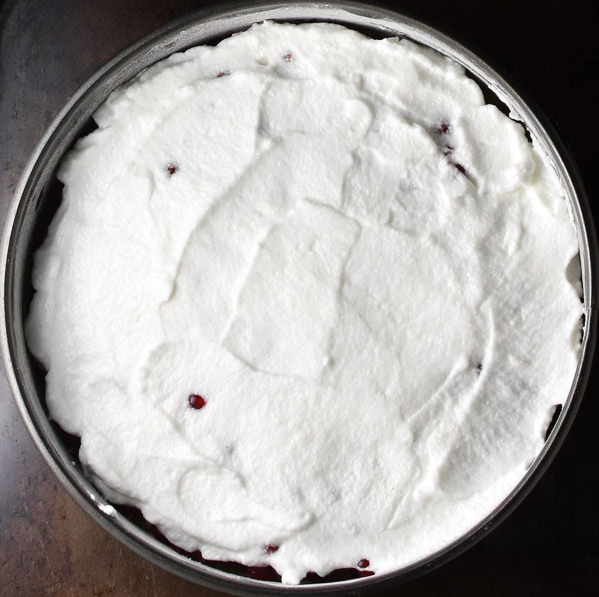 Top down view of beaten egg whites mixture layer in round cake pan.