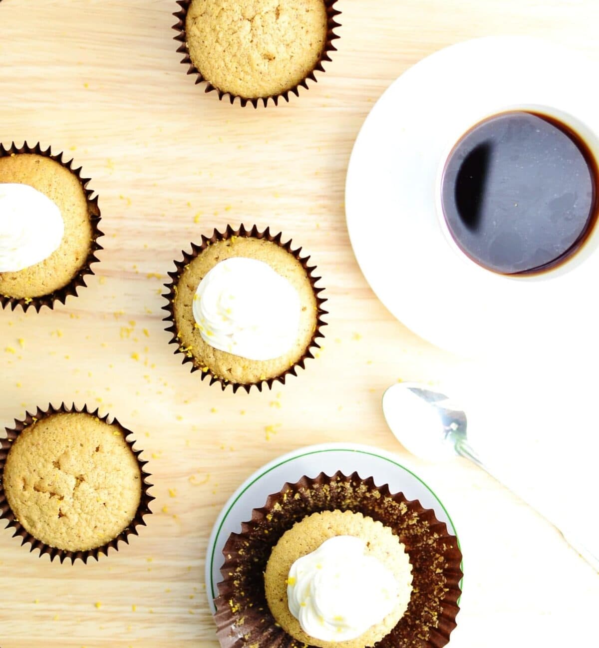 Top down view of cupcakes with white frosting and cup of coffee on white saucer.