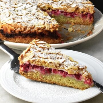 Side view of red currant cake slice on white plate with whole cake in background.