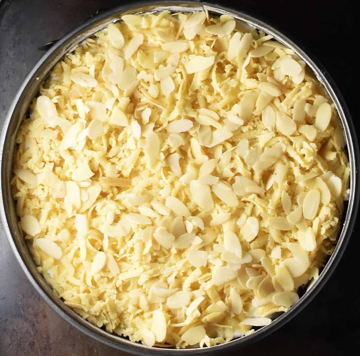 Cake topped with a layer of shredded dough and flaked almonds in pan.