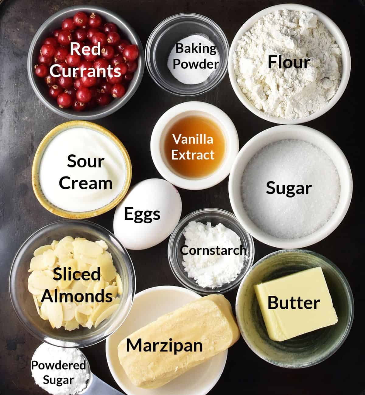 Top down view of red currant cake ingredients in small, labelled dishes.