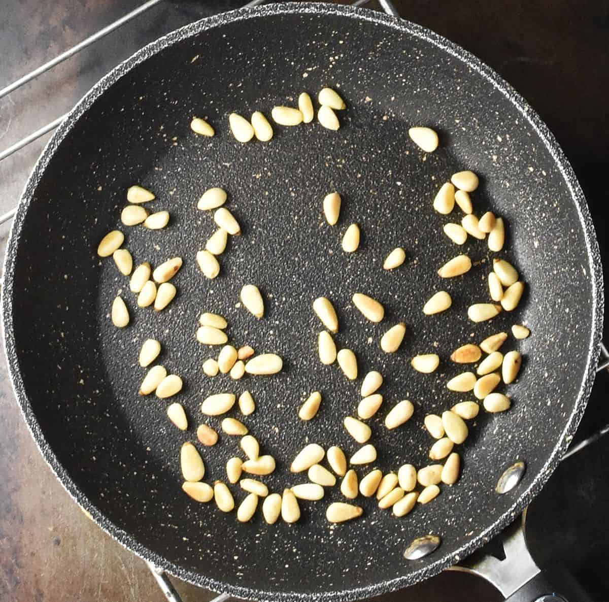 Top down view of toasted pine nuts in black pan.