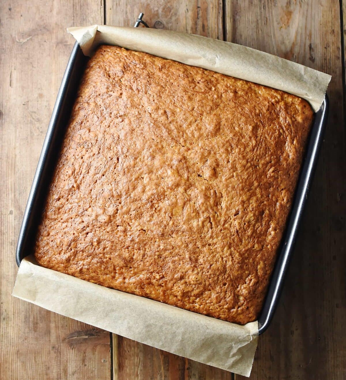 Baked healthy pumpkin cake in square pan with parchment paper visible.