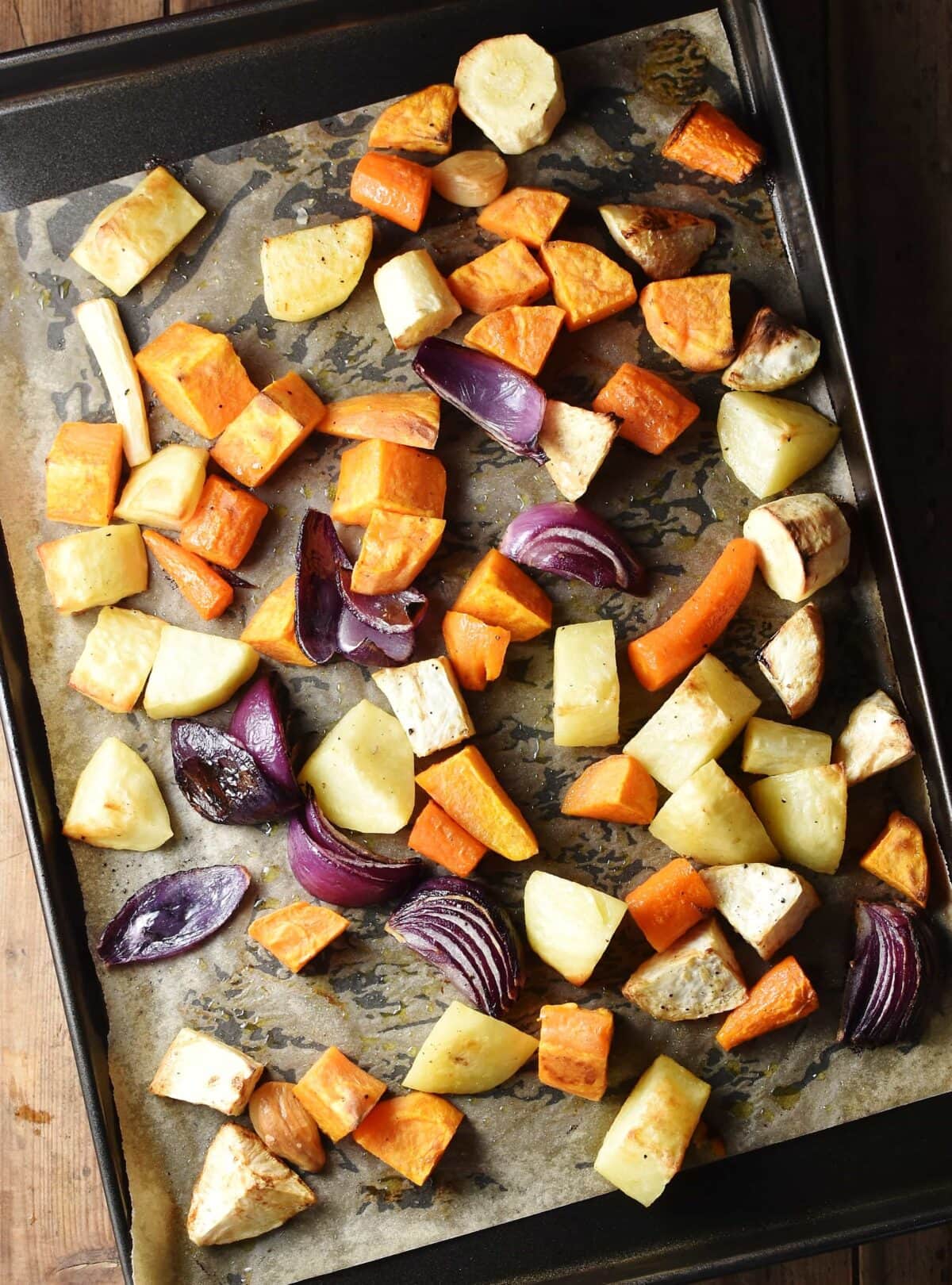 Roasted chunks of root vegetables and red onion on baking sheet lined with paper.